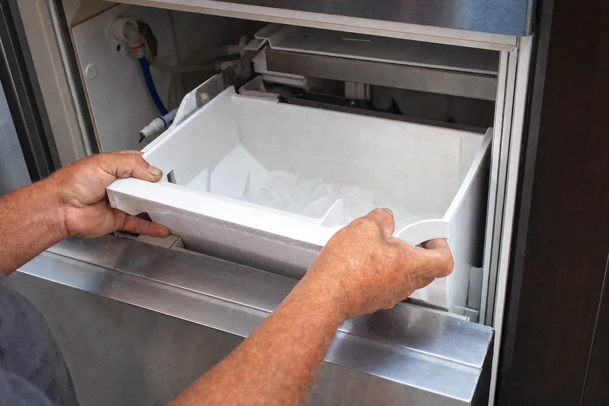 A technician’s hands steadying the plastic bin of an ice machine as it clears the cabinet