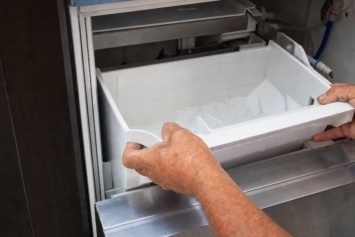 The open front of an undercounter ice machine with the bin partly withdrawn and the stainless door panel swung wide