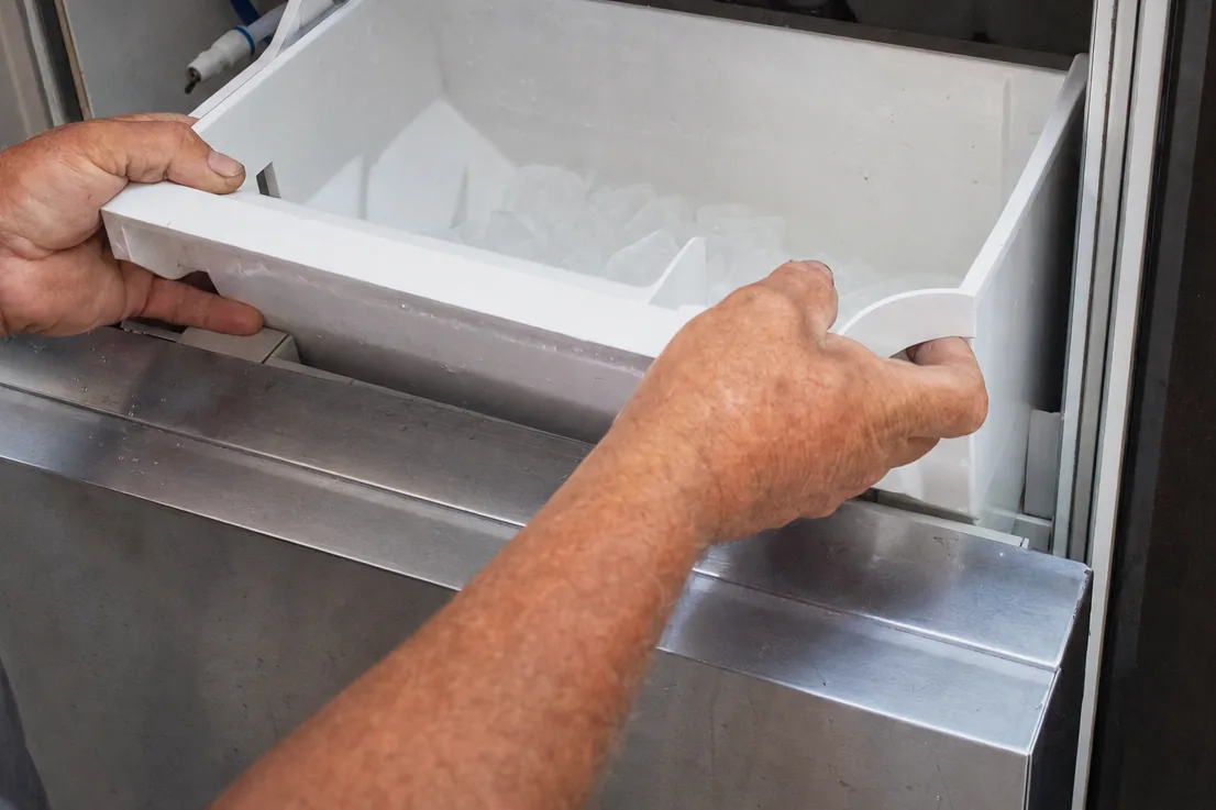Hands holding the ice bin level while it is lifted clear of its runners