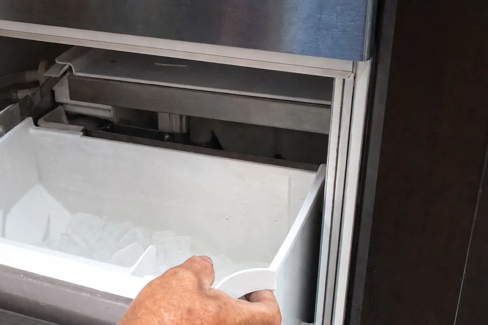 The stainless frame of an undercounter machine with the bin removed, showing the drain trough underneath