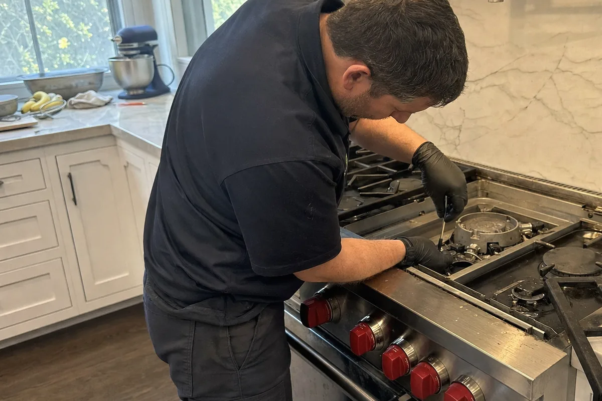 A range set into a marble surround with the wall above it, seen from the side while a technician works at the cooking surface