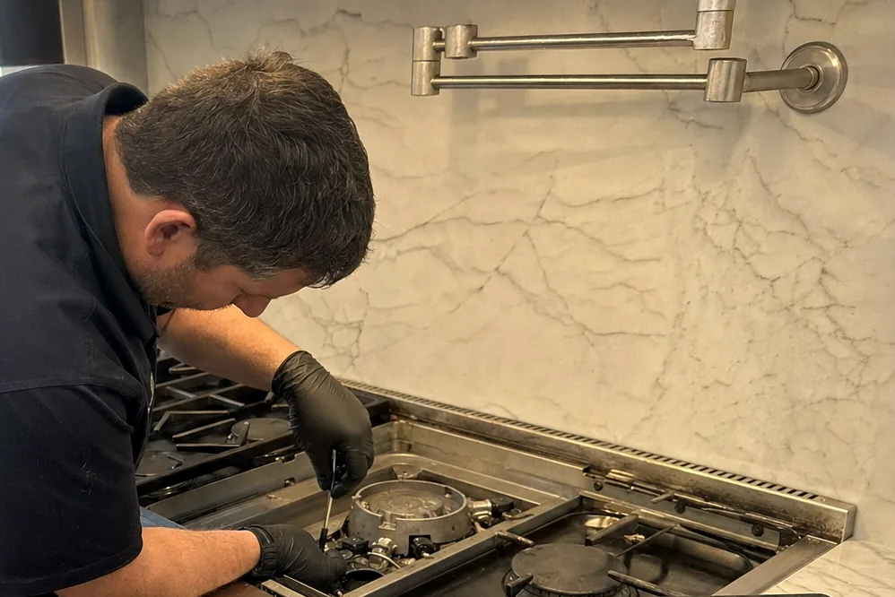 Close view of a professional range front: red knobs, brushed steel, and the technician working just above them