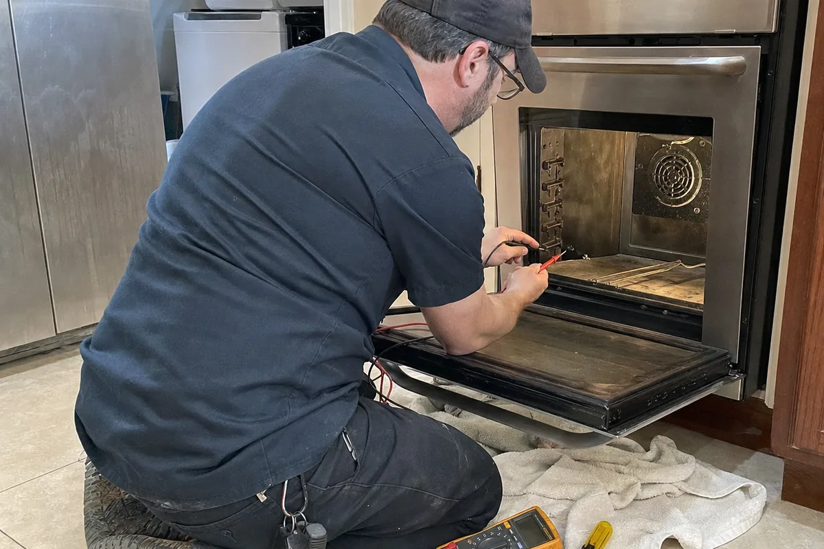 Close view into an open oven cavity with the technician testing at the door hinge and control area
